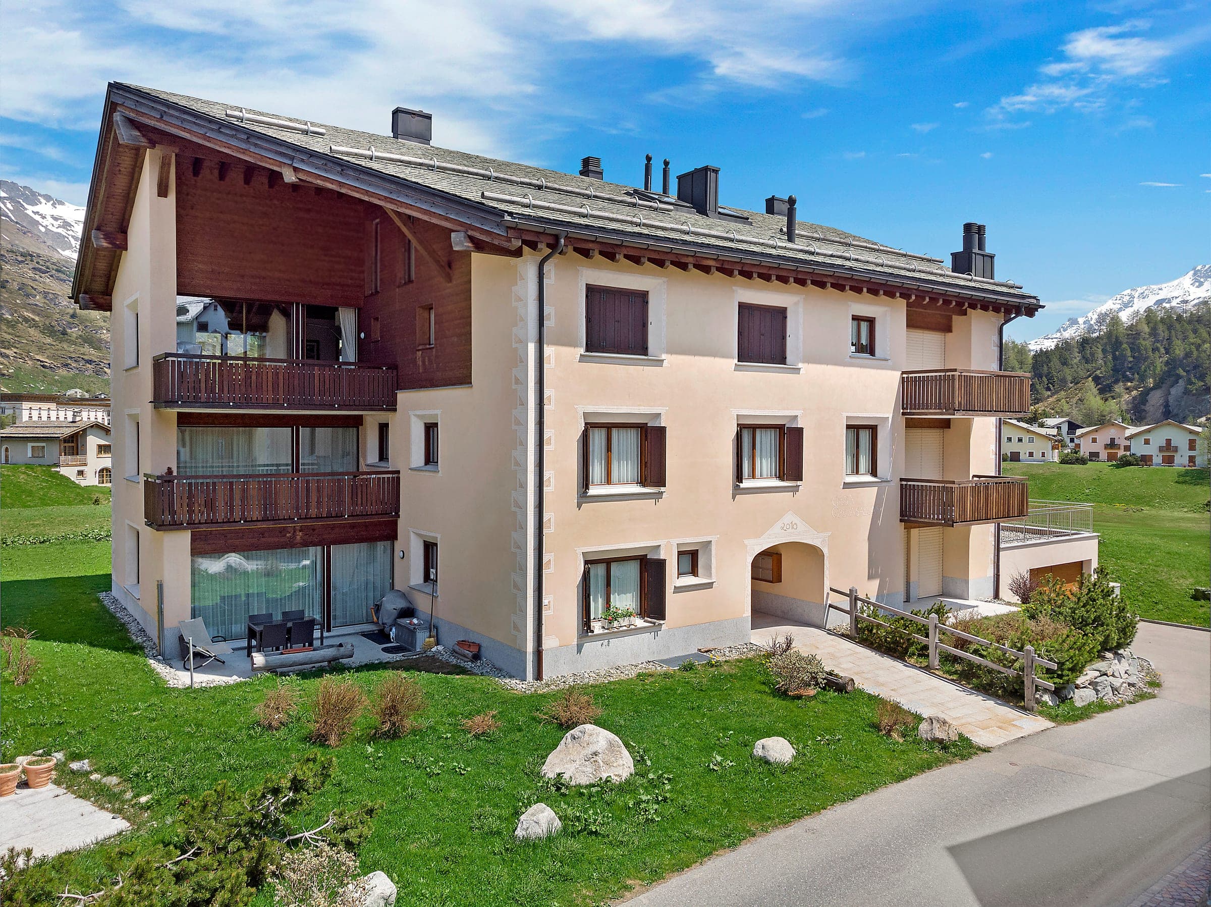 Mehrfamilienhaus im Engadiner Stil, umgeben von Wiesen, von oben