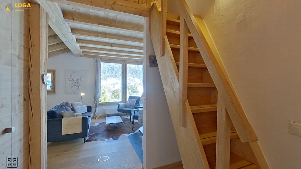 Stube mit Sofa und Holztreppe in einer Wohnung im Engadin